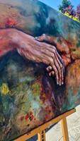 Detail von „Hold Me“: der ausgestreckte Arm und die geöffnete Hand über der hell gemalten Fläche.